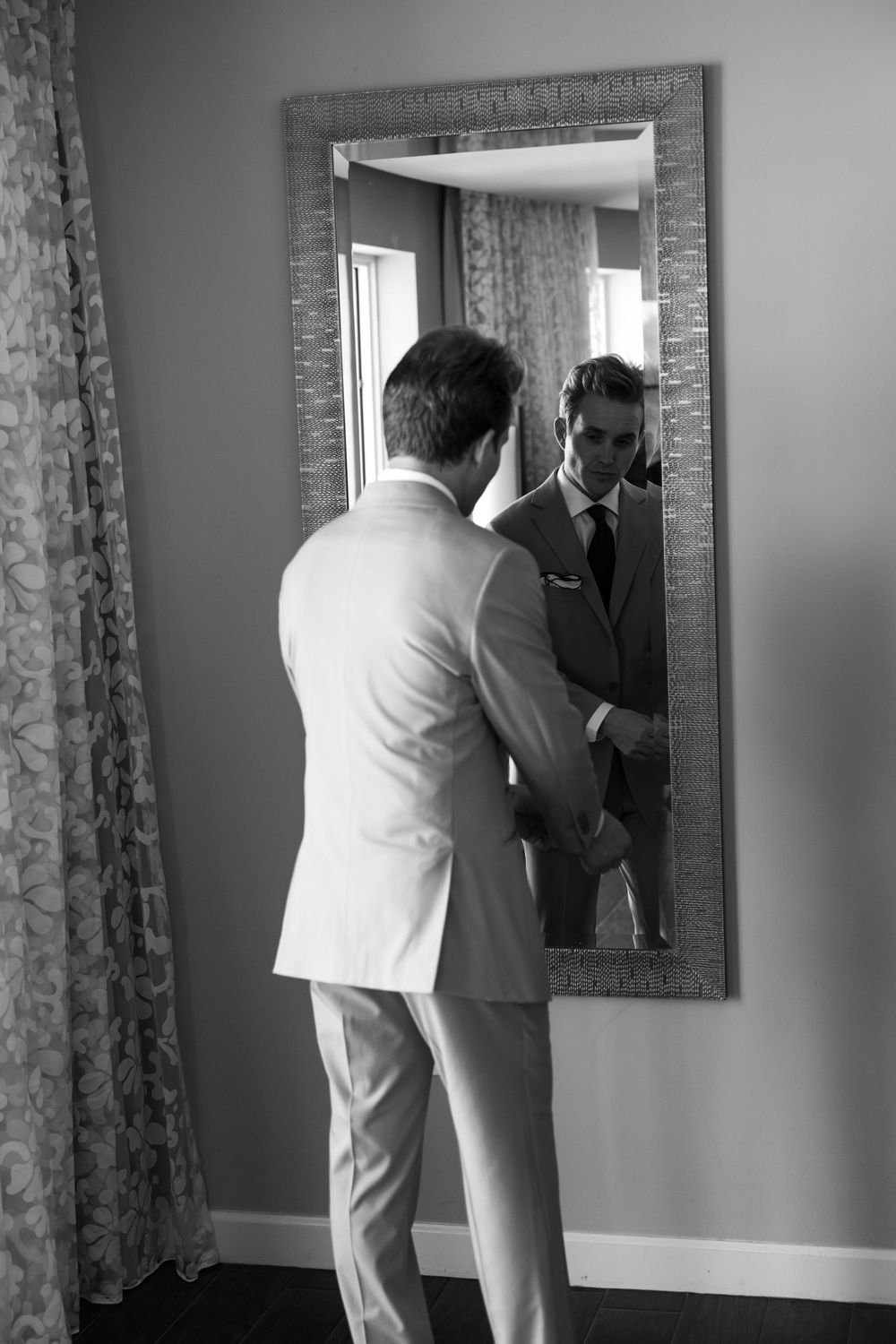Black and white photo sequence showing a person in white suit adjusting their outfit in a wall mirror.