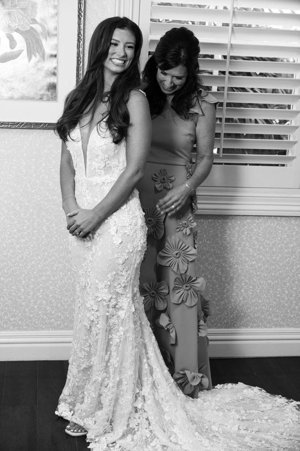 Two figures share a tender embrace while one wears a flowing white lace wedding dress.