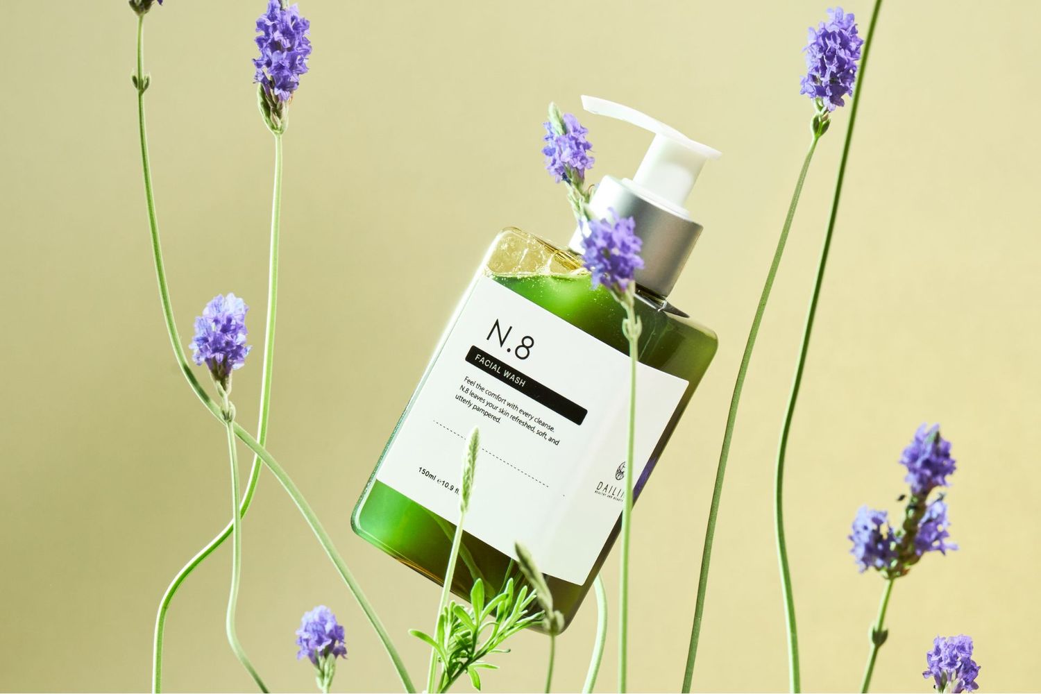 Purple lavender flowers with bottle packaging displayed in soft natural light against pale green backdrop.