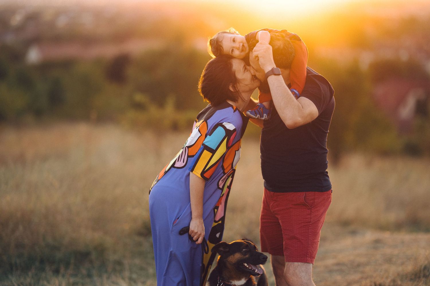 Couple embracing in a romantic sunset moment in a field with warm golden light glowing behind them.