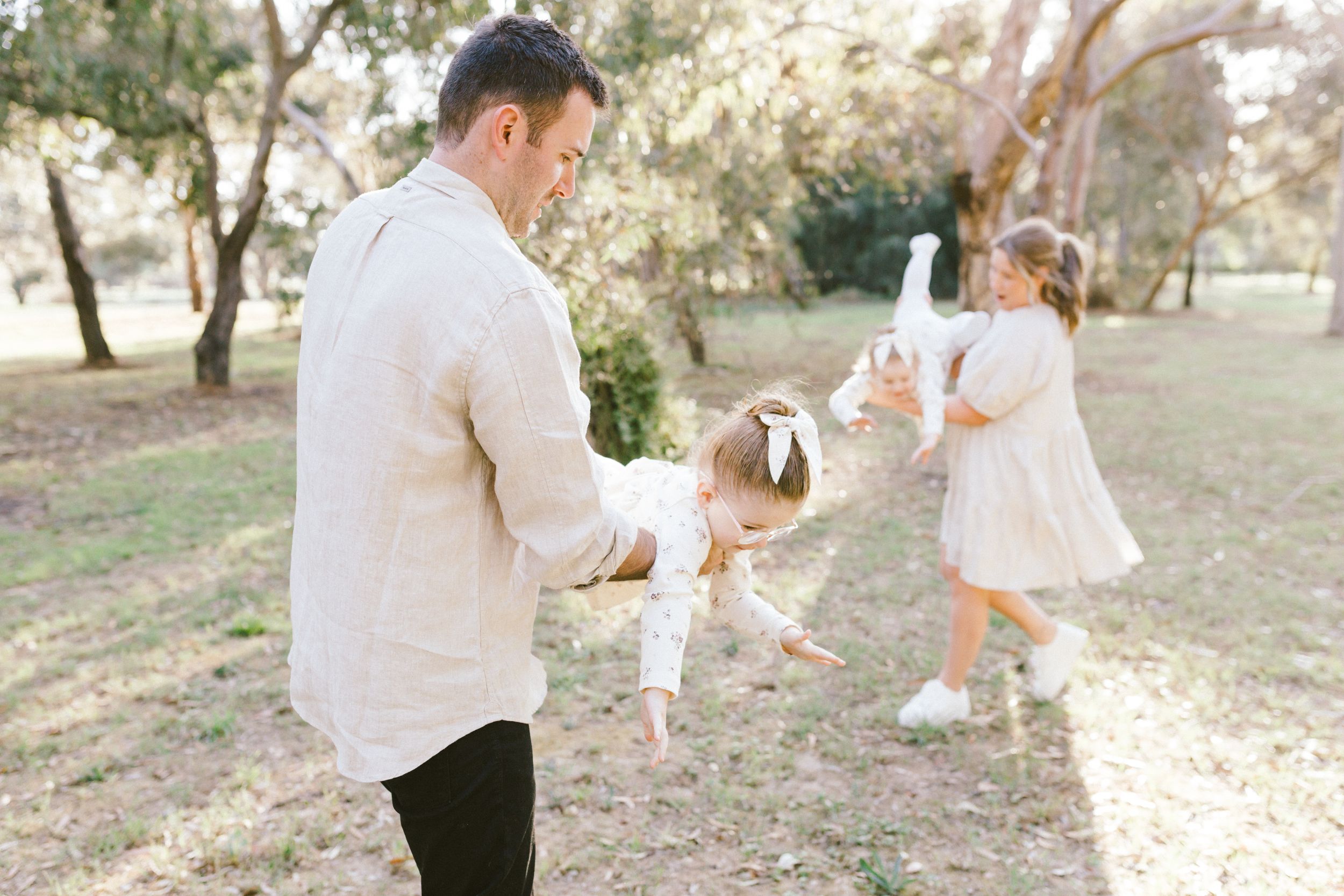 A person in white and peach formal attire walks through an outdoor wooded area in natural lighting.