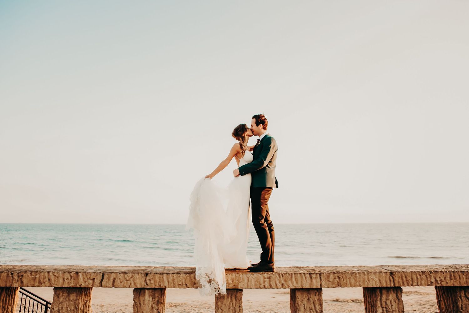 Romantic coastal wedding photos taken on wooden pier at sunset in Orange County, CA.
