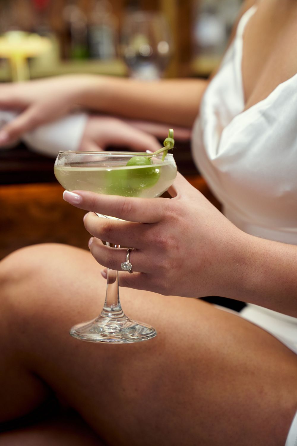 Several elegant cocktail glasses containing martinis with lime garnishes sit on someone's lap while relaxing. Engagement photoshoot