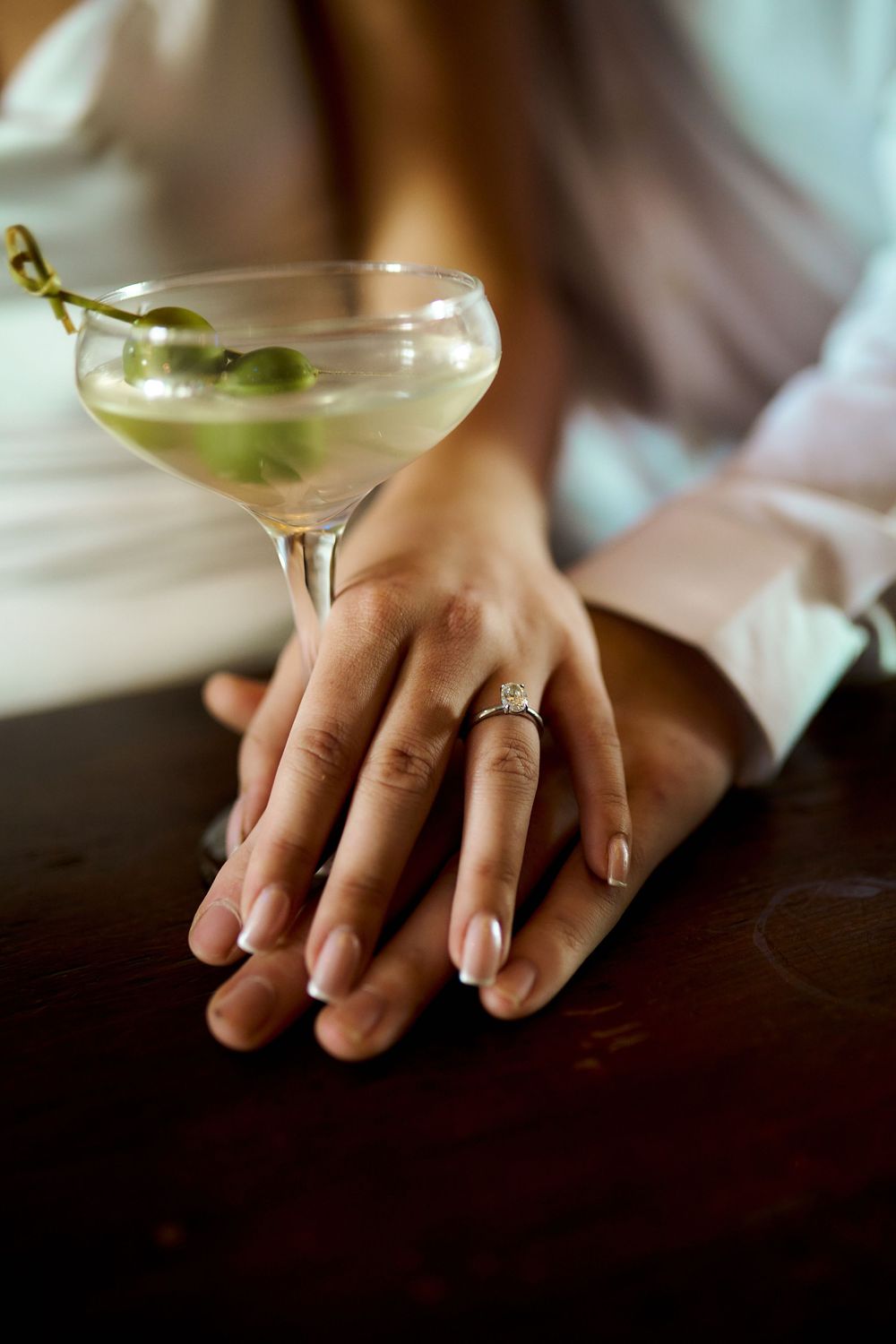 Five martini glasses arranged in a row showcase cocktails with olive garnishes while hands display elegant rings. Engagement photoshoot