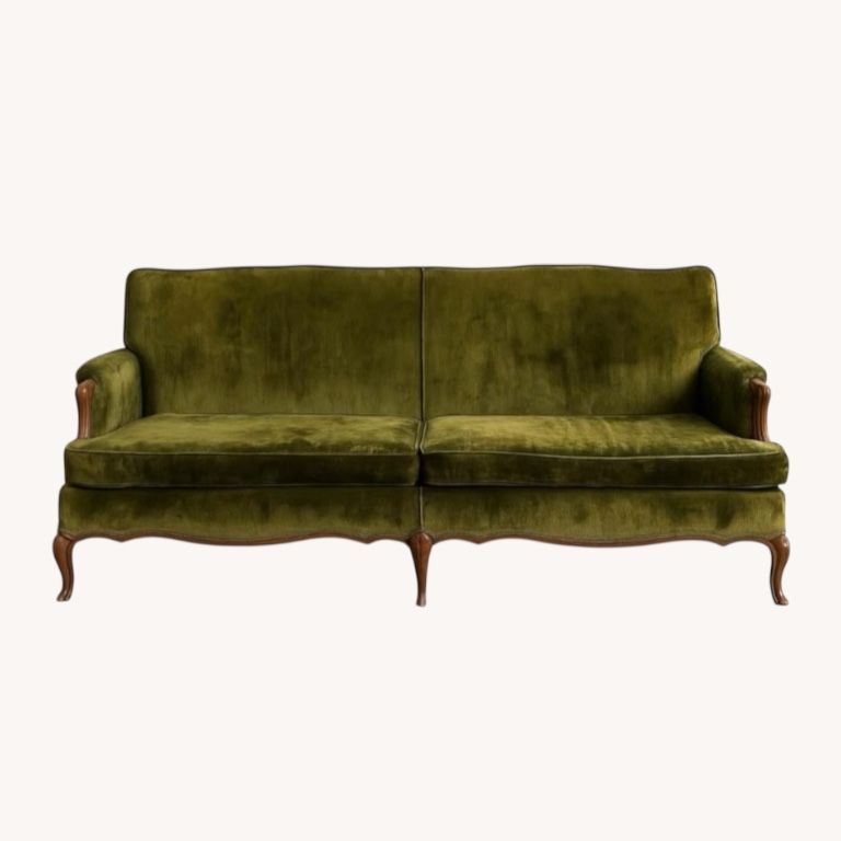 A vintage French-style settee with light gray upholstery and wooden frame sits elegantly on grass with trees in background.