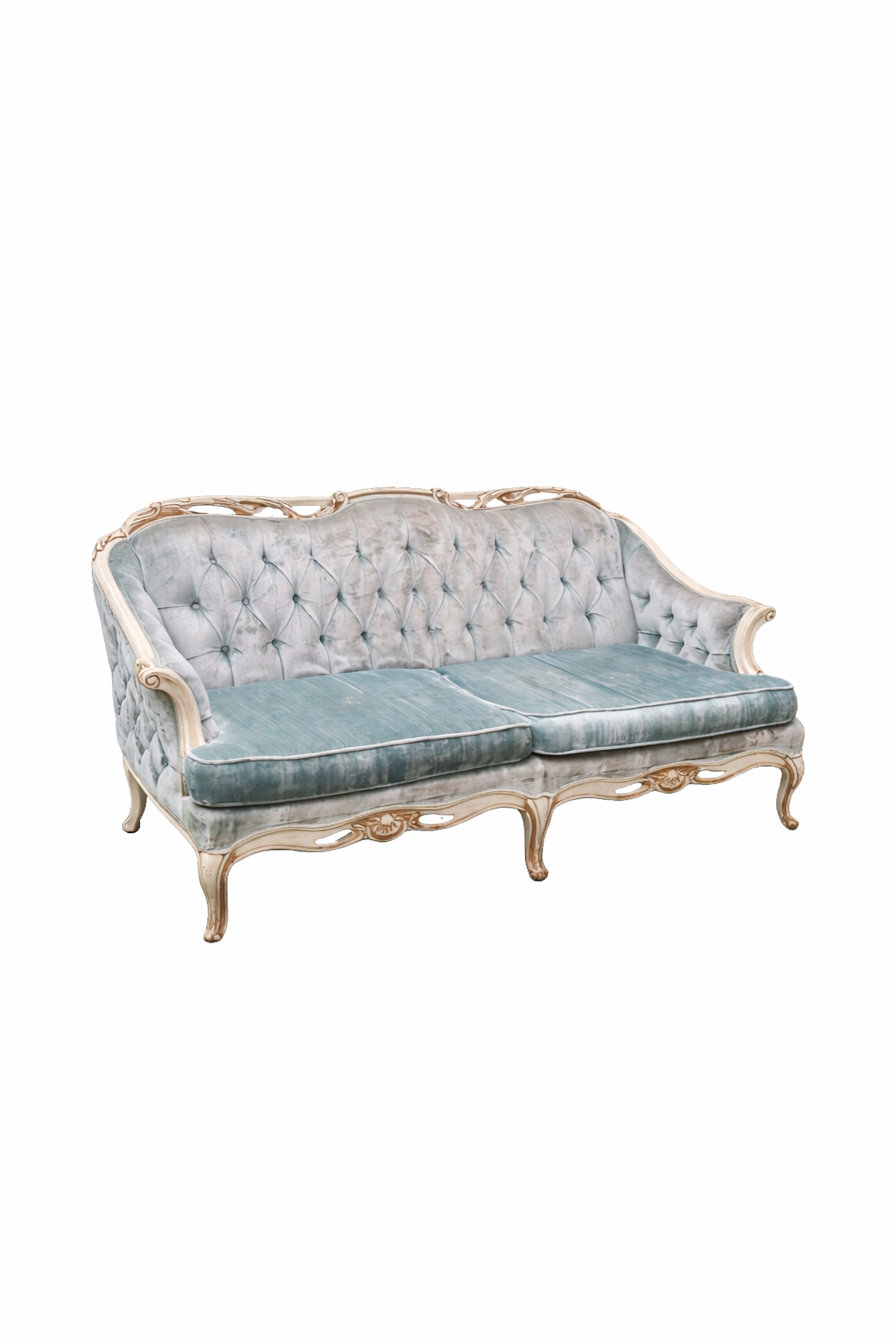 A vintage French Provincial style sofa with tufted velvet upholstery in blue-gray sits on grass against green foliage.