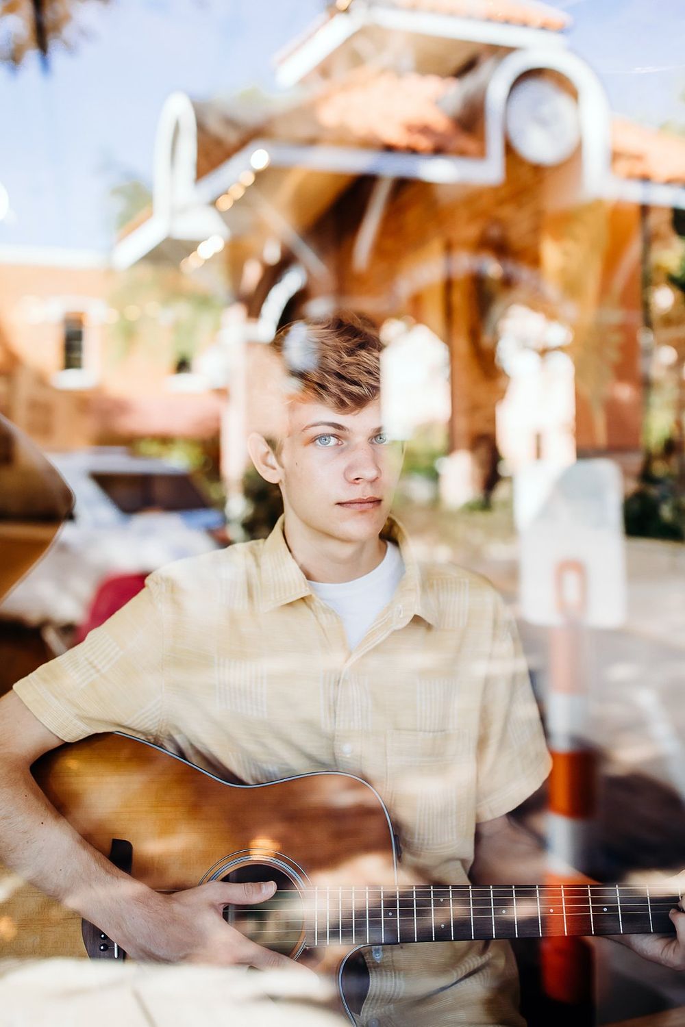 Teen musician practices acoustic guitar on sunny patio with warm lighting and blurred background effect.
