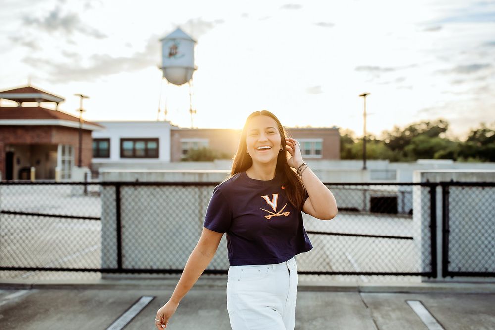 A person wearing casual clothing sits alone on a concrete barrier in an urban setting during sunset hours.