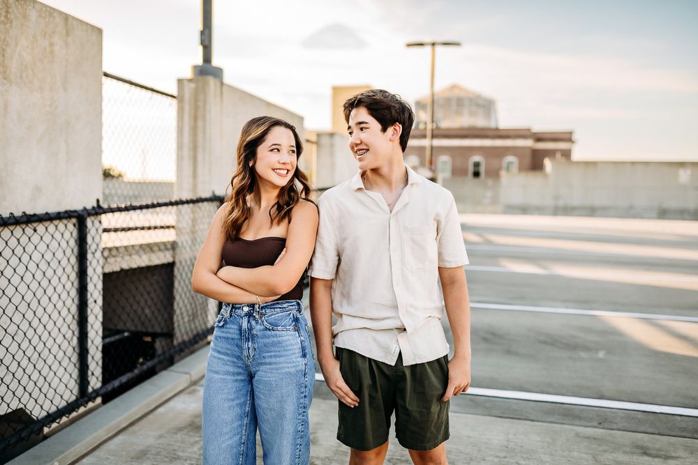 A couple enjoying a casual rooftop date wearing coordinated white shirts and denim in urban setting at sunset.
