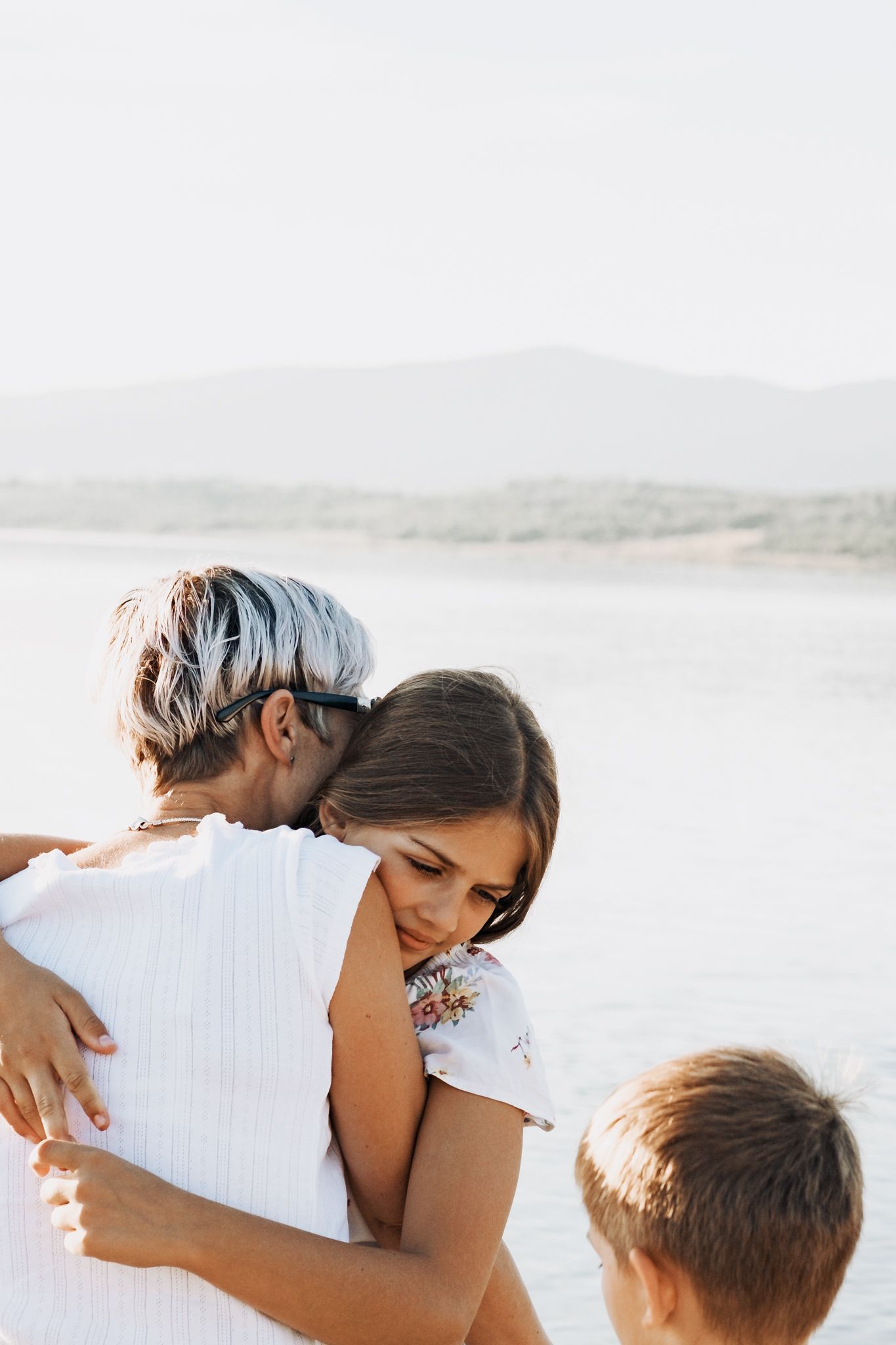 Family embraces on a bright sunny beach with calm water in background.