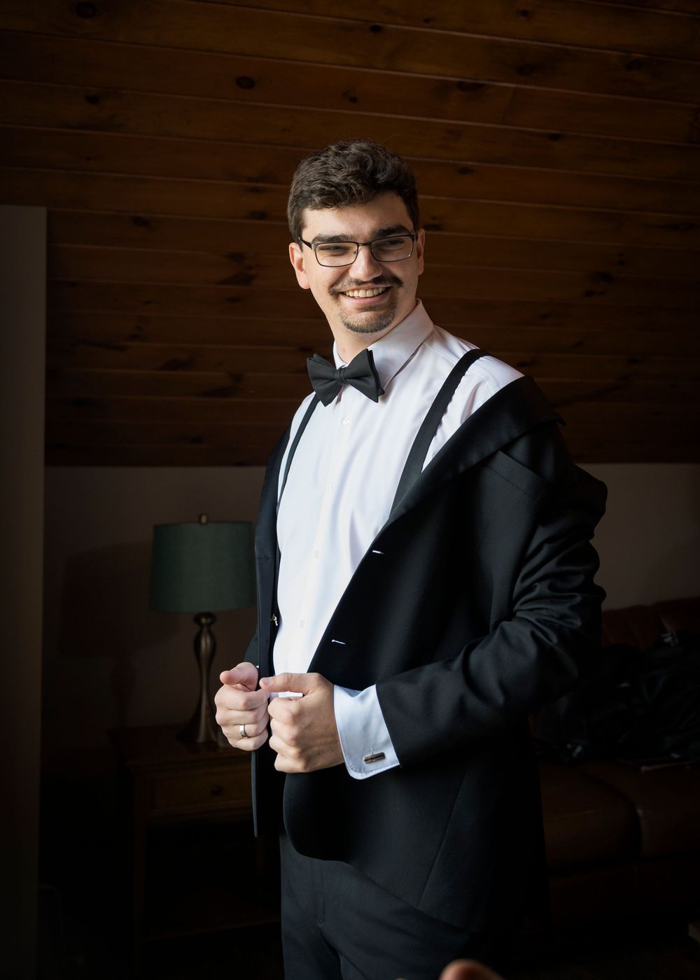 Someone wearing a formal black tuxedo and white shirt straightens their bowtie.