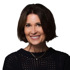 Portrait of someone wearing a black knitted sweater and short dark hair, smiling warmly against white background.