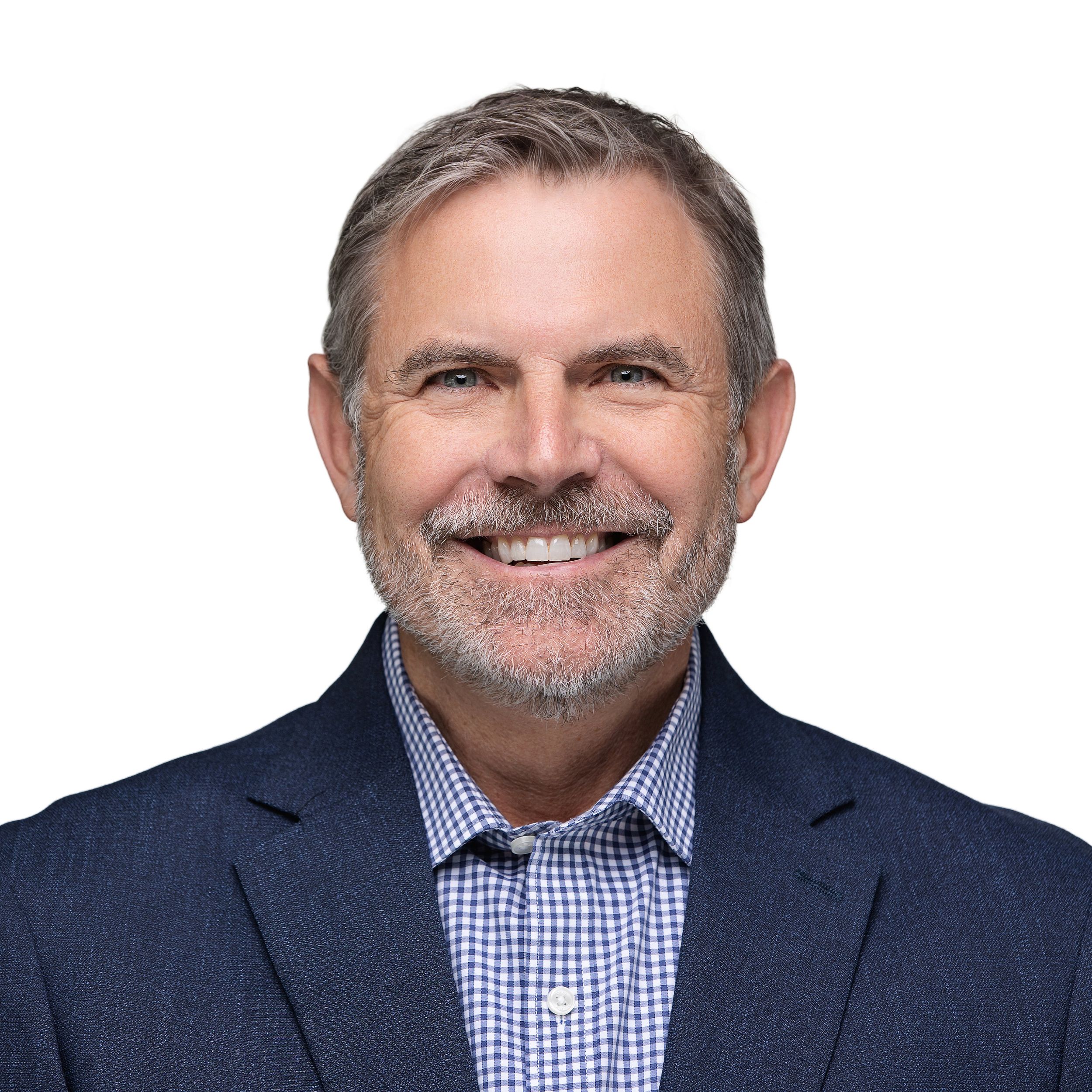 Professional headshot of person in navy suit and blue gingham shirt smiling against white background.