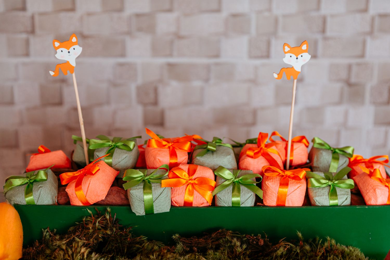 Orange carrot-shaped favor boxes with green paper leaves arranged in a row on a green tabletop at a party.