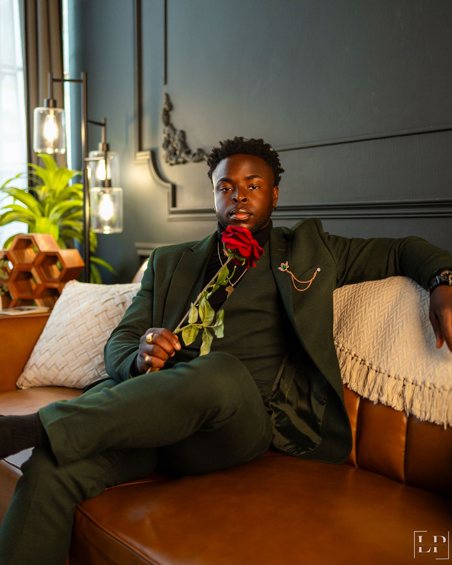 Professional portrait in a dark modern office setting with leather couch and plants.