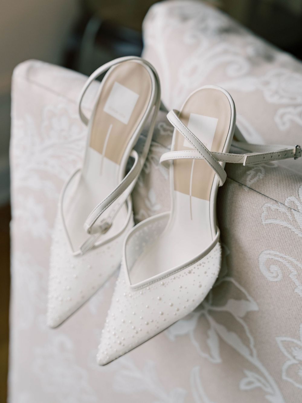 Elegant white bridal shoes with delicate beading displayed on lace fabric.