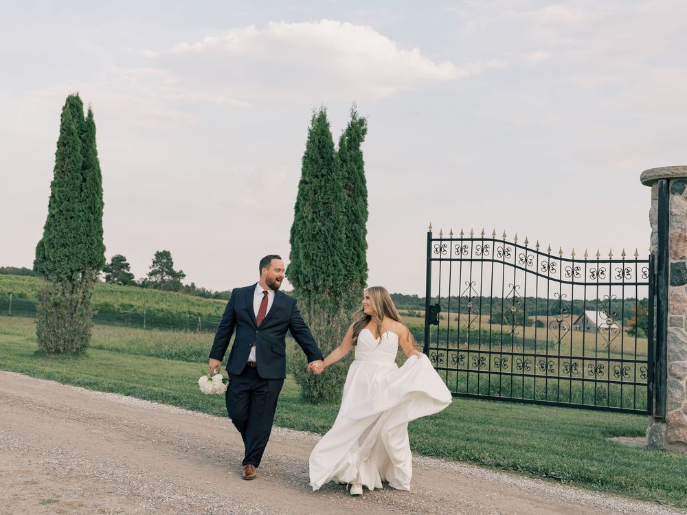 A couple walks together along a path lined with cypress trees and an iron gate.