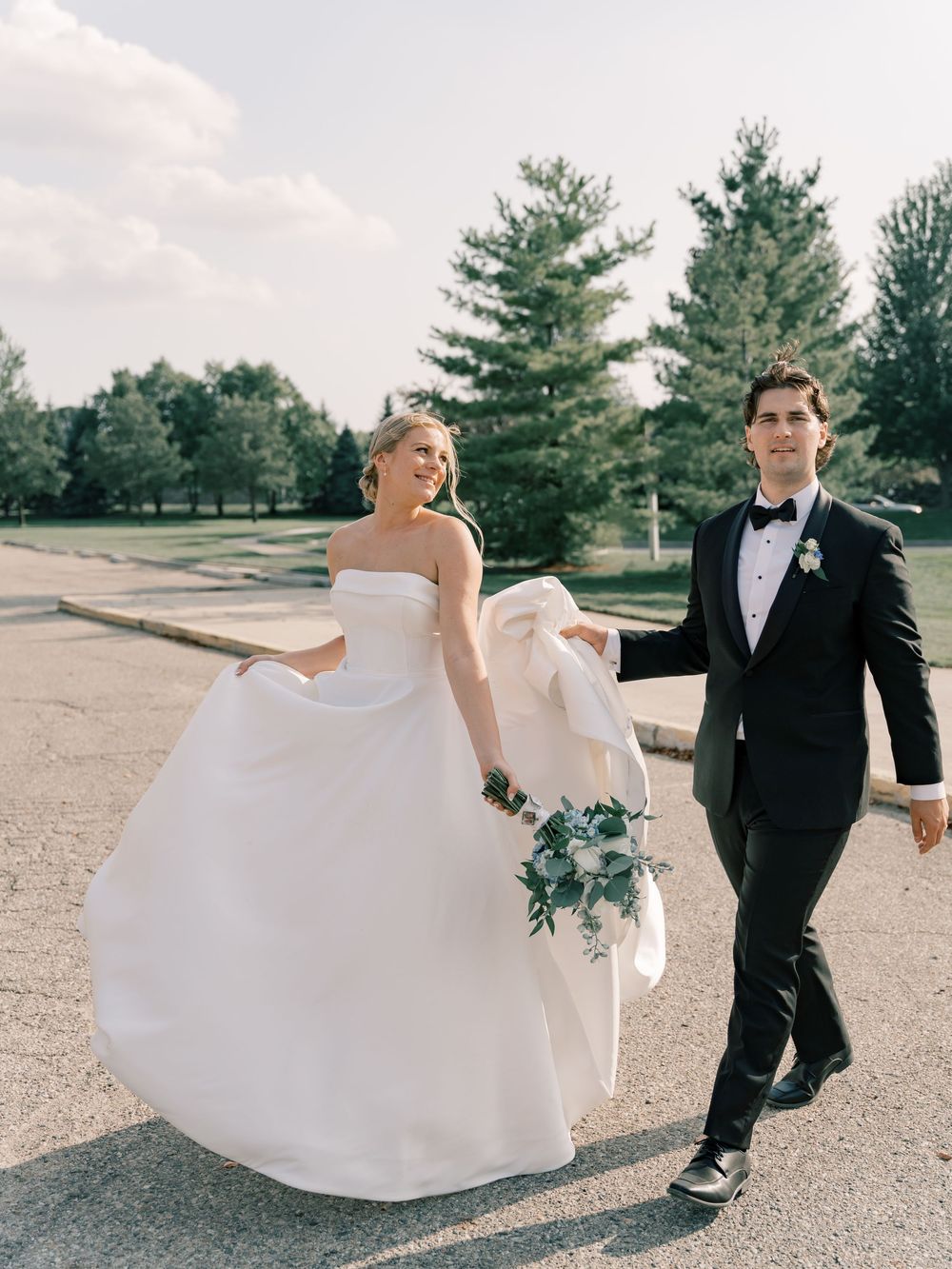 Couple walking on gravel path with flowing white wedding dress in motion.