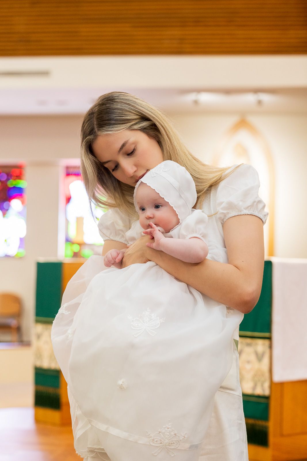 A tender moment with a baby in a long white baptismal gown being held and kissed in a church.