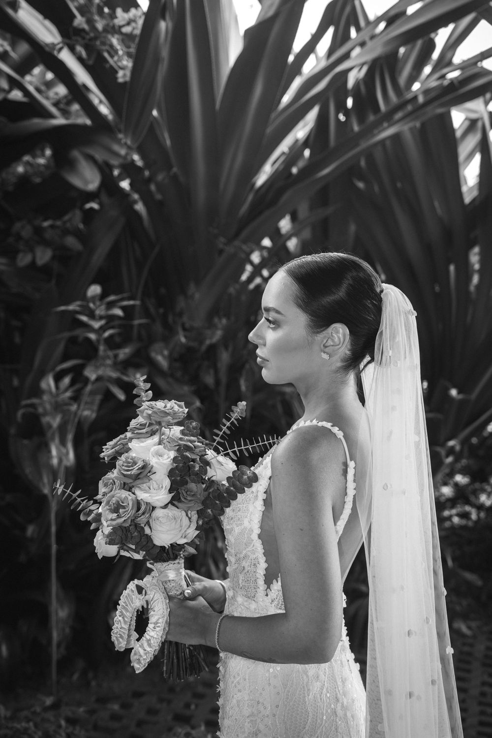 Black and white romantic bridal portrait series showing wedding dress details and floral bouquet against tropical foliage.