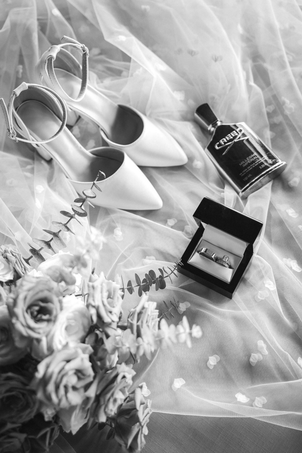 Wedding accessories including white shoes, perfume bottles, and delicate flowers arranged on flowing tulle fabric.