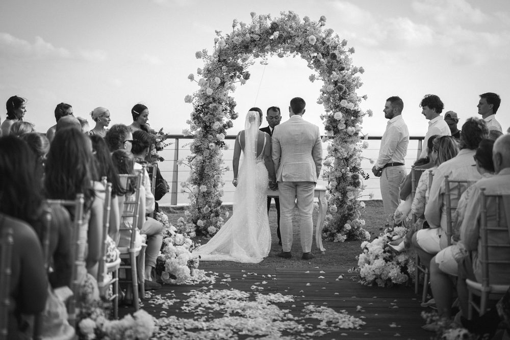 Black and white photo montage showing guests gathered at an elegant outdoor wedding ceremony under floral archways.