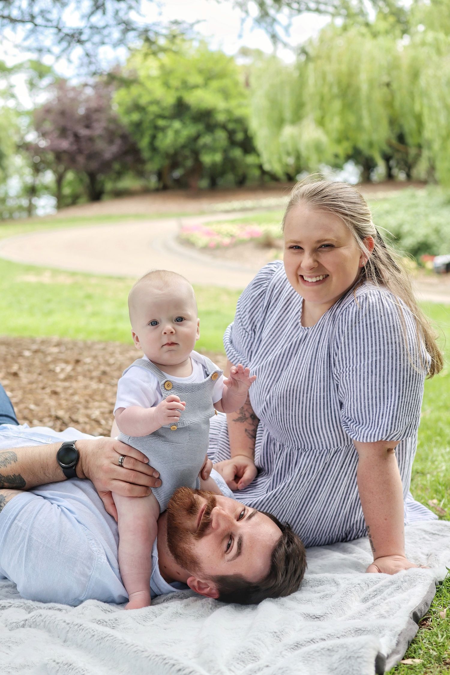 Young couple with a baby boy lying down on a picnic blanket in the park.