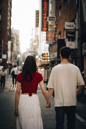 A couple in white and red clothes walking hand in hand down a city street with Japanese signage.