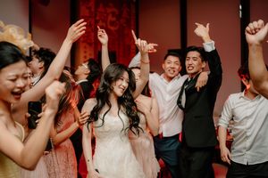 A joyous dance party moment at a wedding reception shows guests celebrating with raised arms on a dimly lit dance floor.