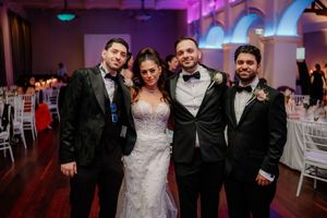 Wedding party poses together on dance floor under dramatic purple lighting at reception venue.