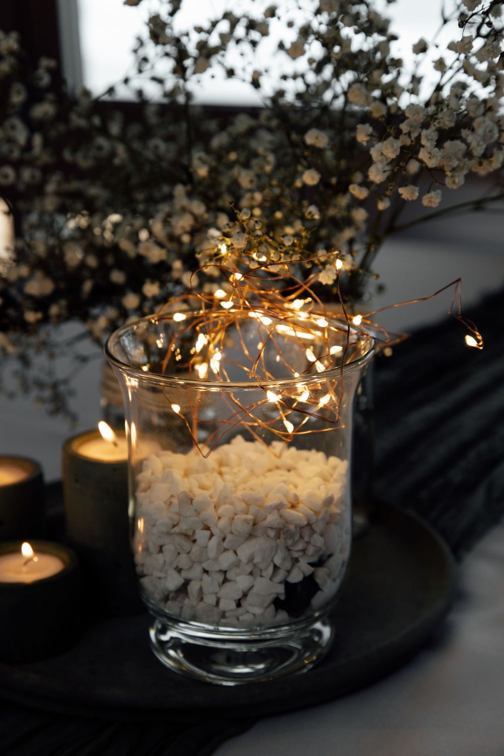A string of warm fairy lights illuminates delicate baby's breath flowers in a glass bowl creating a cozy winter decoration.