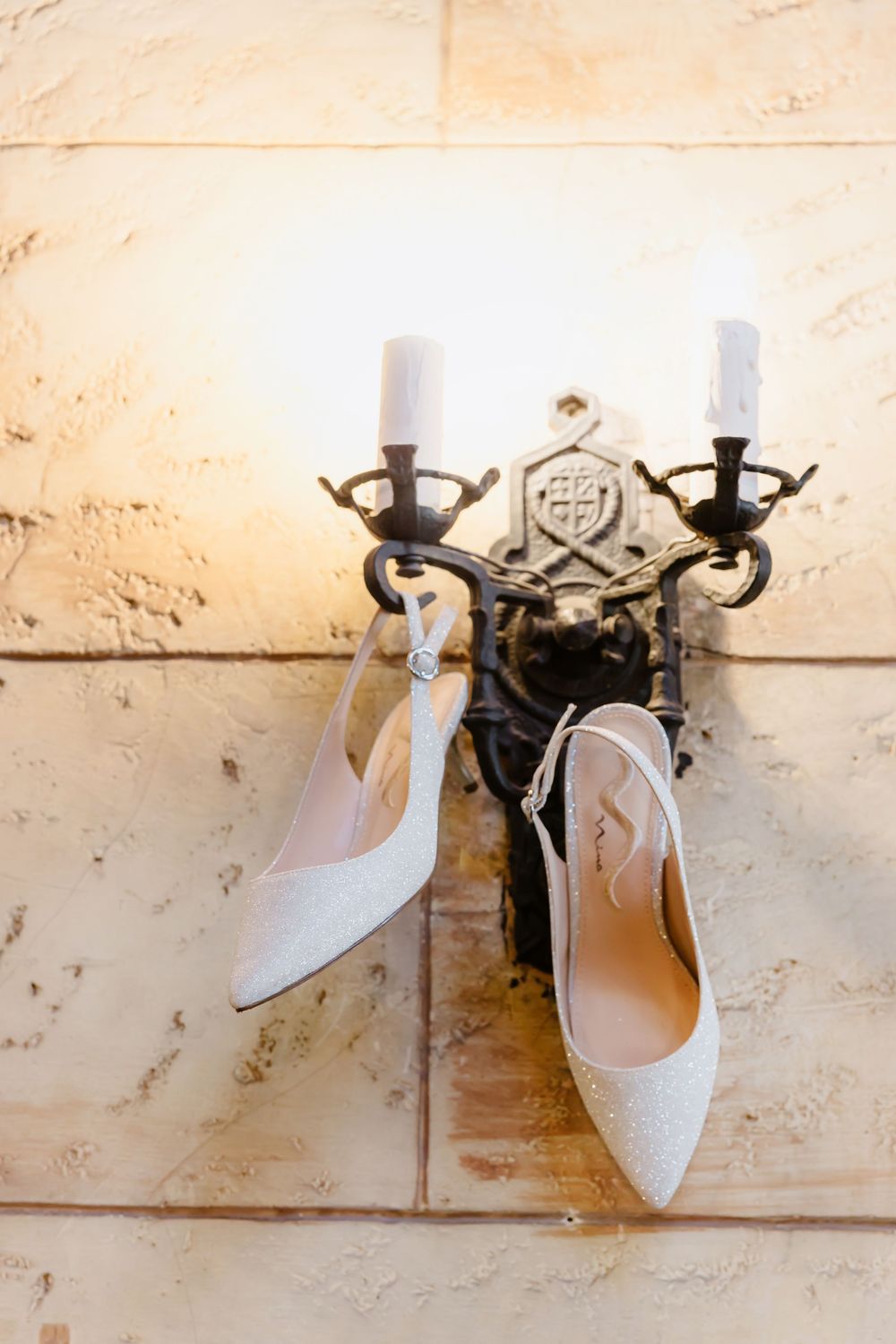 Elegant white bridal slingback heels displayed on rustic wall hooks.