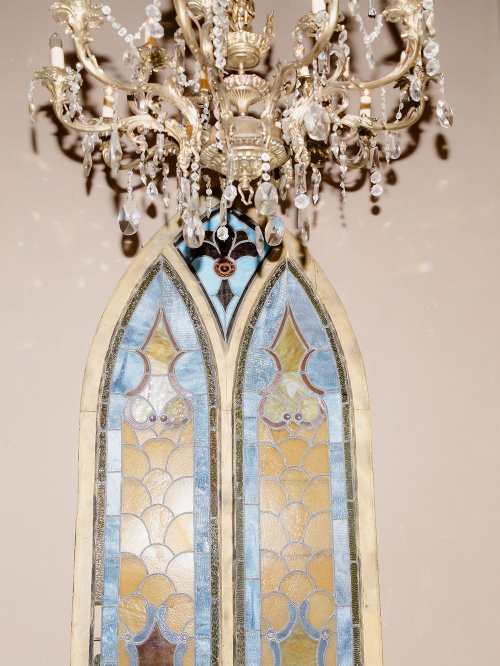 Ornate crystal chandelier hangs above mirrored wall panels with decorative blue and gold painted architectural details.