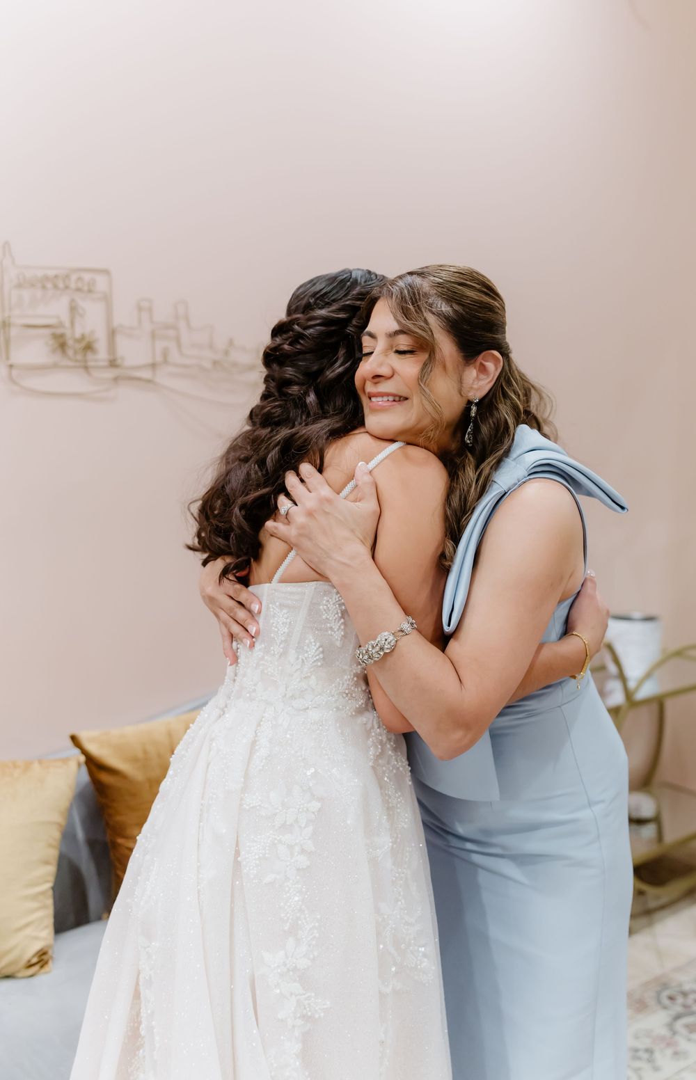Bride in a white gown sharing an emotional moment with someone in a light blue dress during wedding preparations.