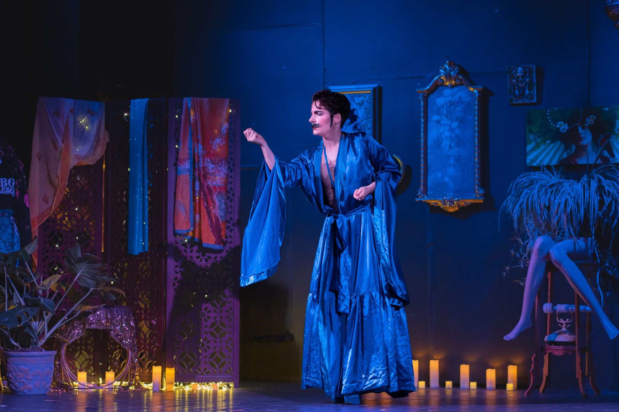 Performer in flowing blue robe gestures dramatically on stage with candles and decorative mirrors. Quad Cities Event Photography