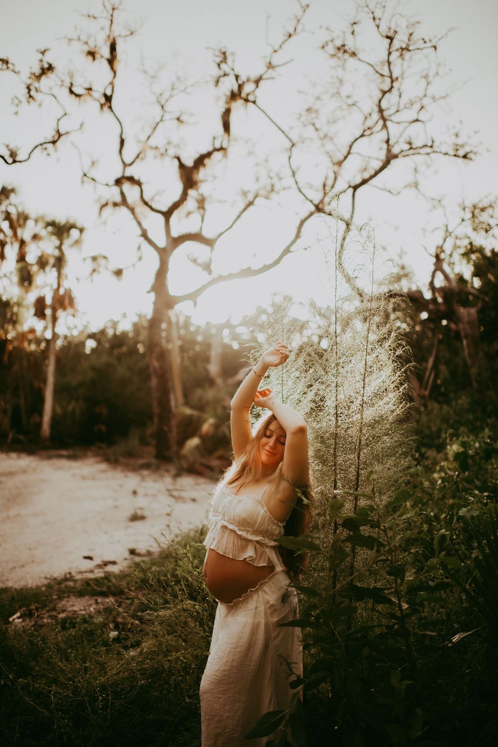 A person in a cozy sweater stands among bare winter trees at sunset creating a dreamy silhouette effect. sarasota family photographer
