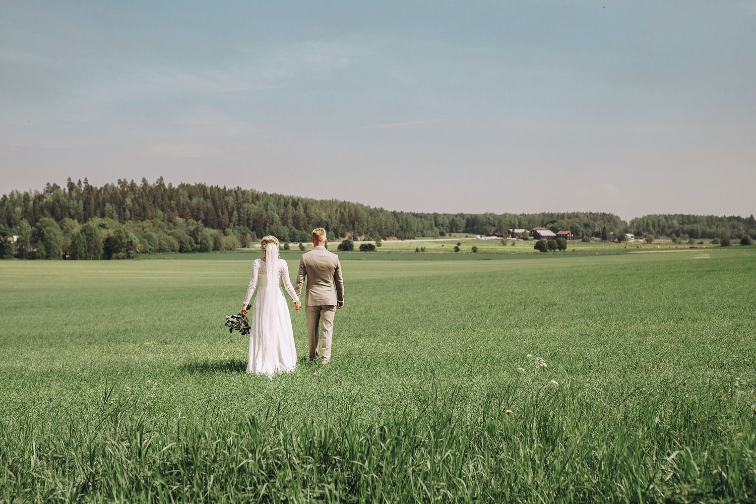 Ett brudpar som går hand i hand på en äng med ryggen mot kameran