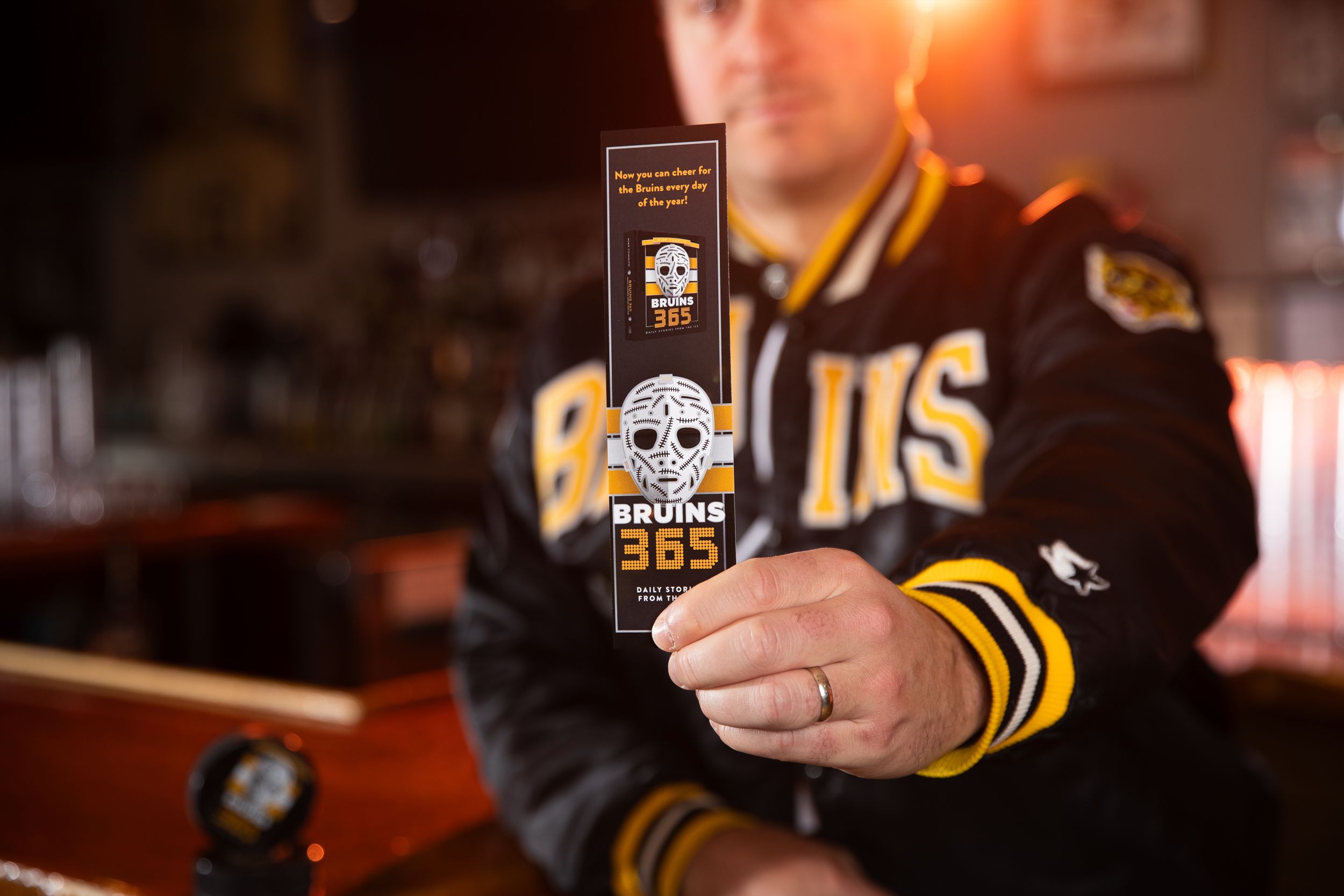 A hockey fan in a Boston Bruins jersey holds up a bottle of Bruins branded beer at a bar.