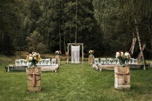 Outdoor wedding venue setup with wooden cross and floral arrangements in a forest clearing.
