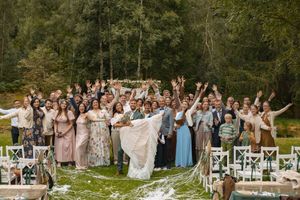 Large group wedding photo with guests celebrating outdoors on a sunny day.
