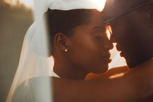 A bride and groom share an intimate moment, bathed in warm golden sunlight, with the bride wearing a white veil.