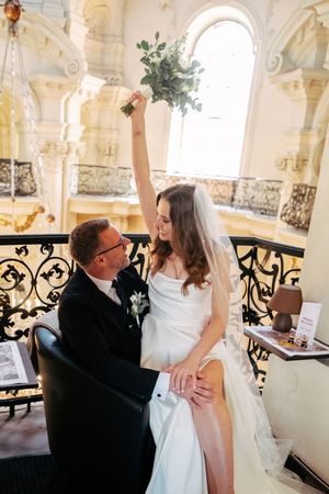 Wedding couple embracing under elegant white stone archways with ornate railings.