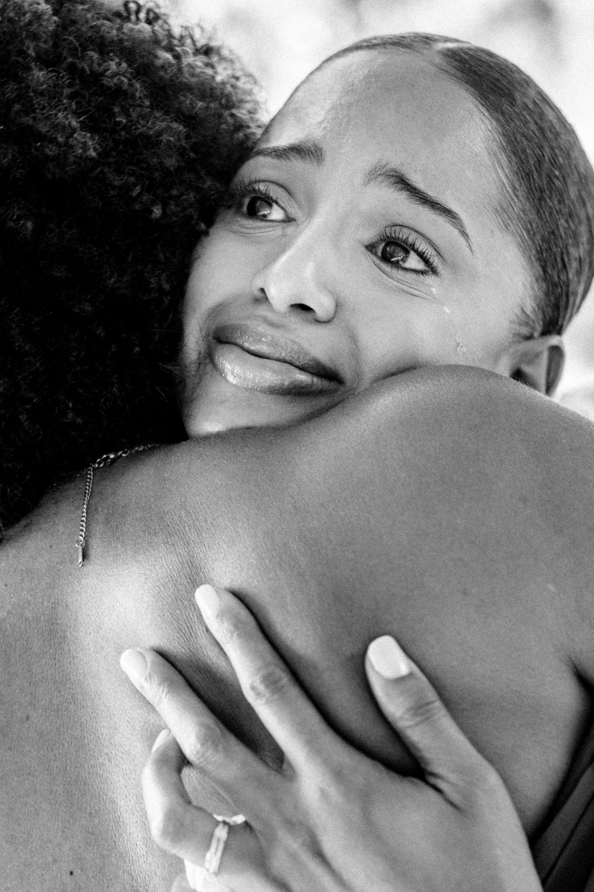 Black and white photo of a woman crying tears of joy while embracing someone, wearing a ring on her finger.
