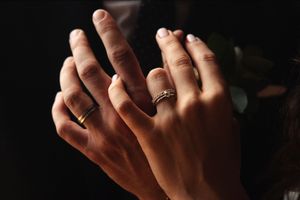 Close up detail of hands with wedding rings in dramatic lighting.