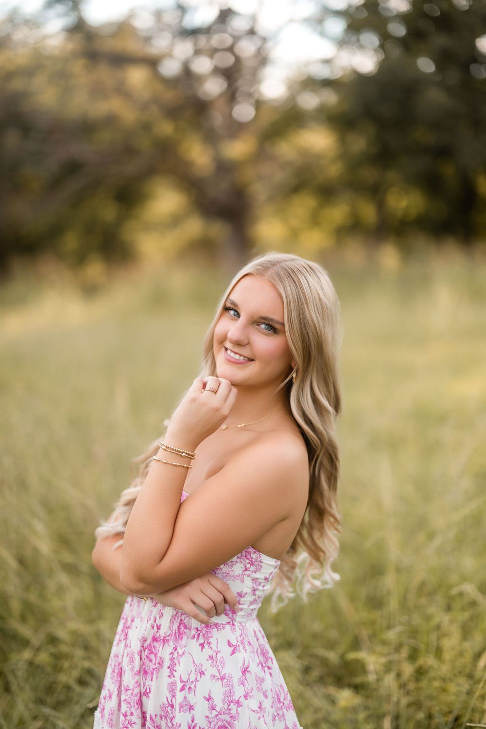 Pink floral dress glows in warm evening light against a natural outdoor backdrop.