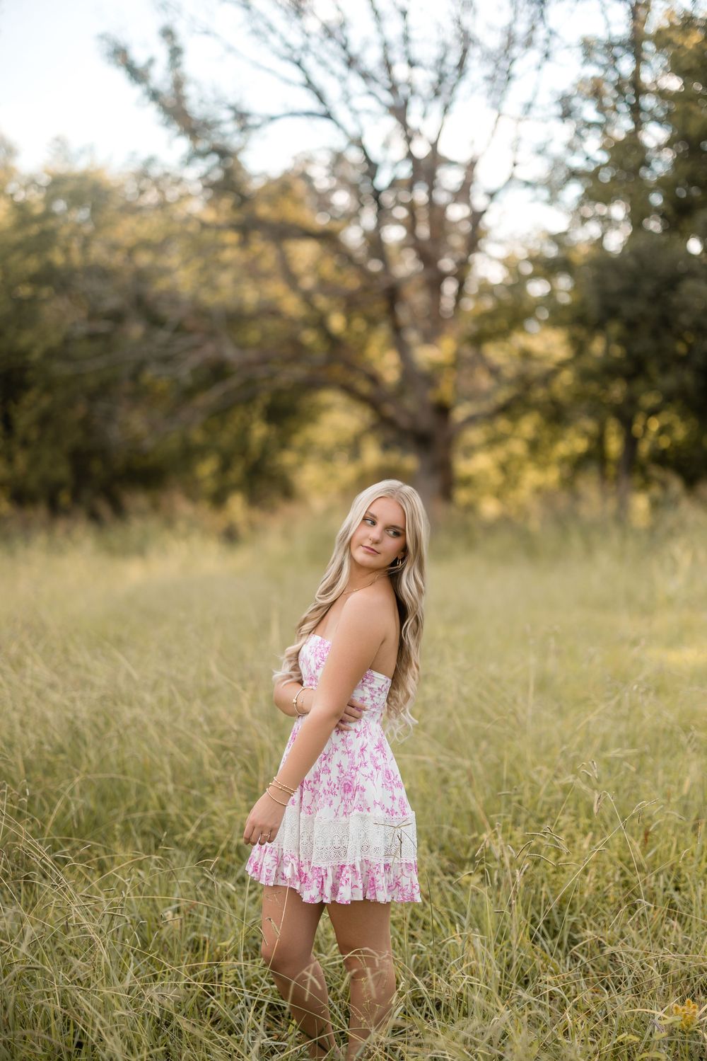 A flowy pink floral dress catches the sunlight in a grassy summer field at golden hour.
