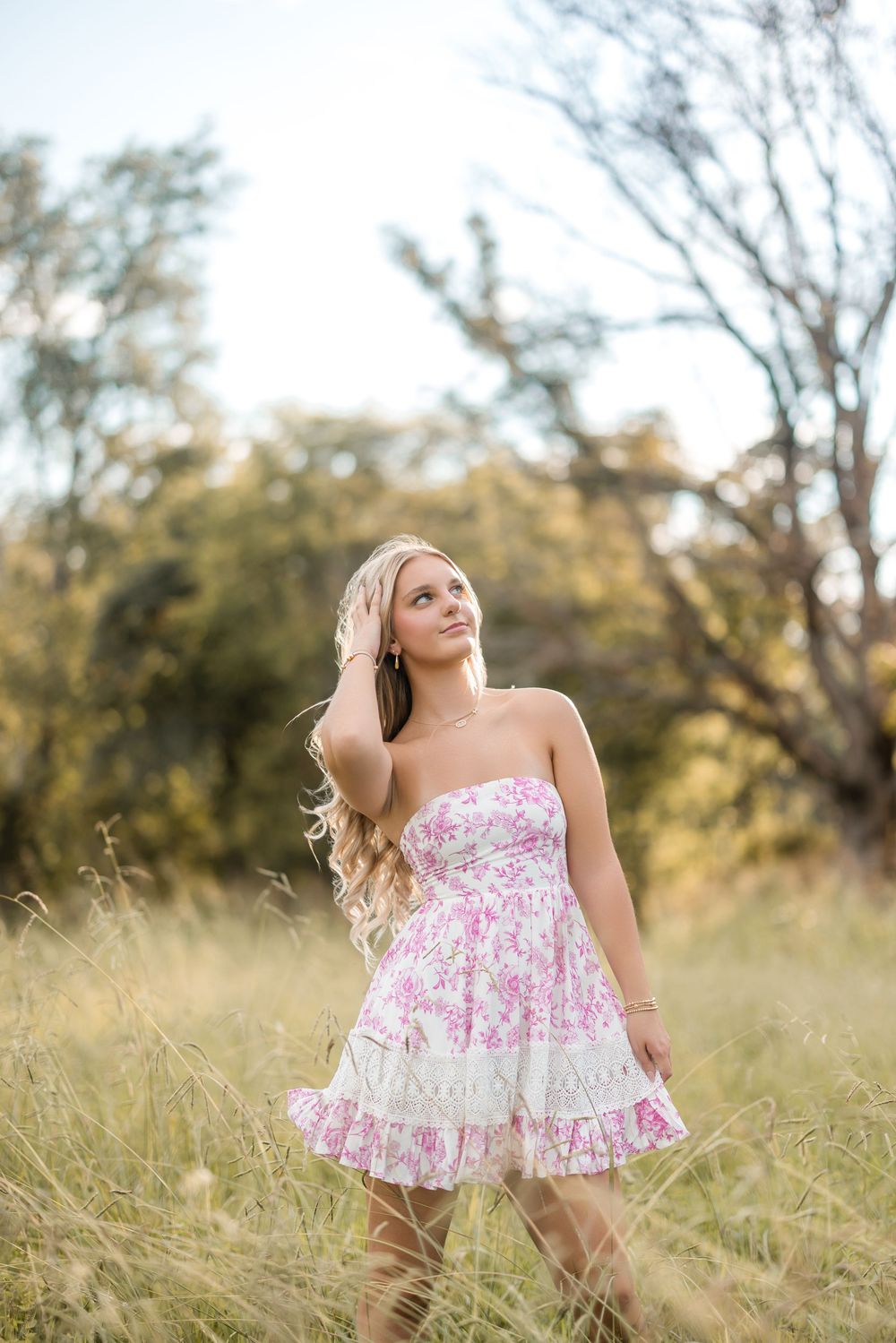 A dreamy summer photoshoot showing someone in a pink floral dress twirling joyfully in a sun-lit meadow with tall grass.