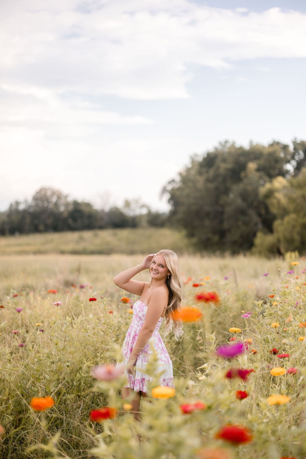 A person stands in a vibrant wildflower meadow with red, orange and pink poppies blooming in the sunlit countryside.