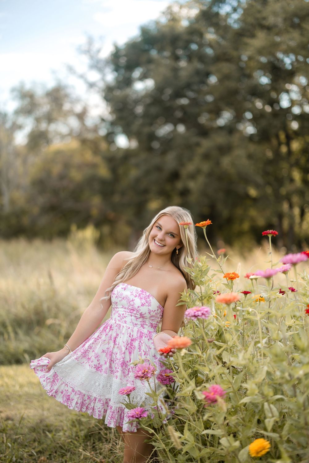 Young woman in a pink floral dress poses playfully among vibrant orange and pink wildflowers in a summer field.