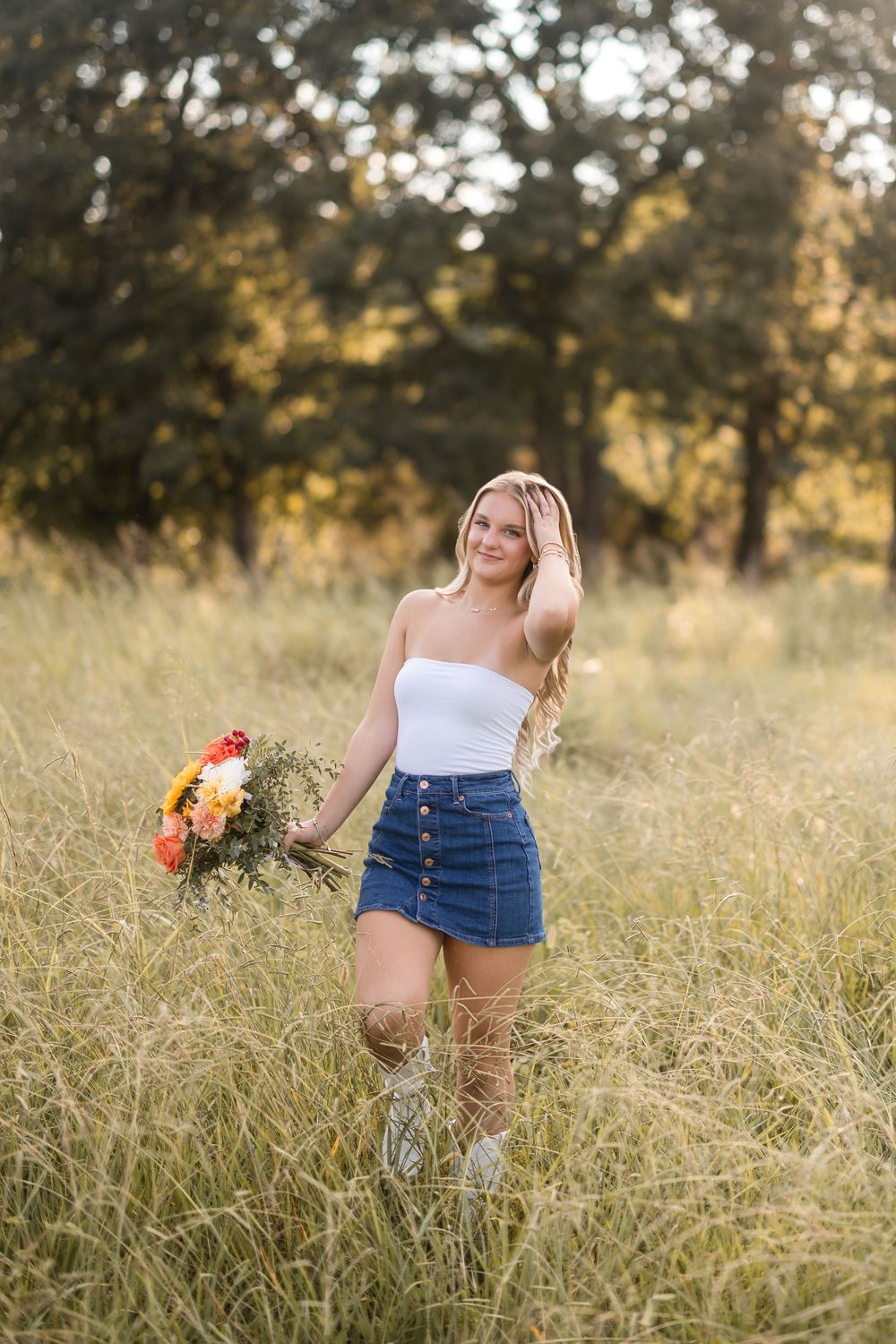 Candid outdoor portrait in a tall grass meadow with denim and flowers during sunset.